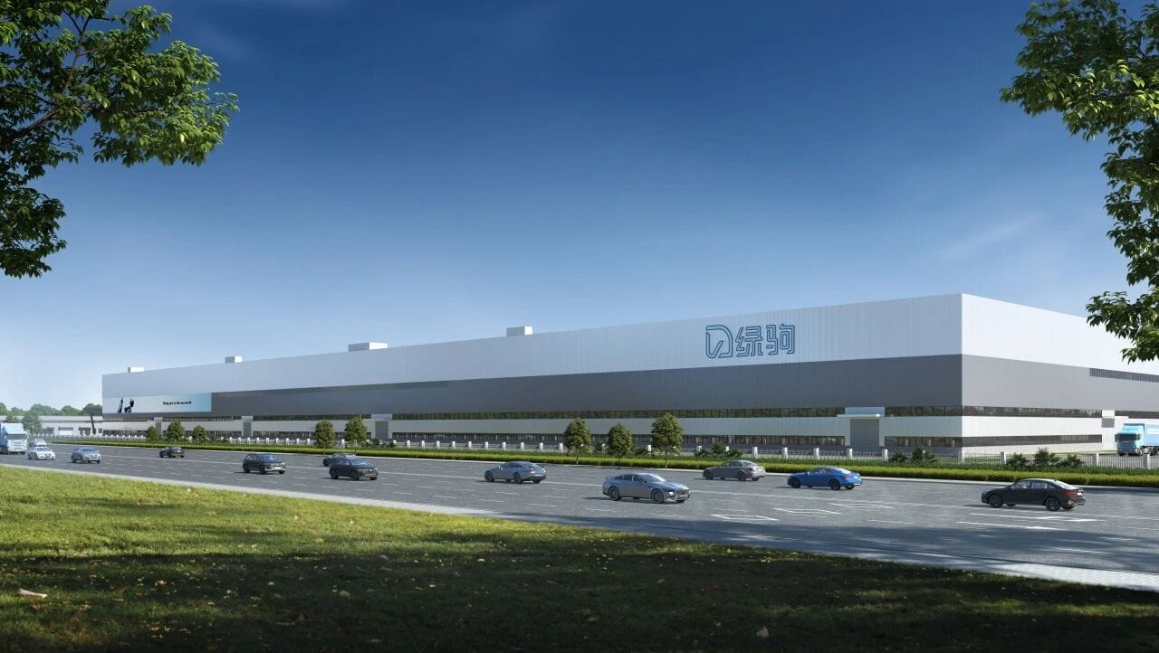 A large, modern retail store in Cambodia with a sleek white facade, situated along a busy road with multiple cars, surrounded by green trees and a clear blue sky.